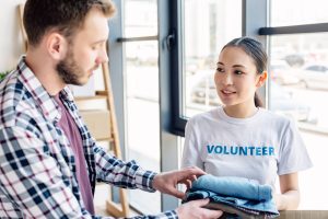 selective focus of pretty asian volunteer giving clothes to man